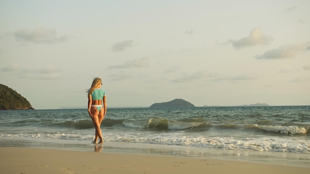 Sexy vrouw die alleen op strandkustlijn loopt en warme gouden ontspant