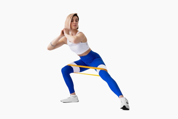 Sexy vrouw in sportkleding die een weerstandsband gebruikt in haar oefeningsroutine Jonge vrouw voert fitnessoefeningen uit op een witte achtergrond Isolate