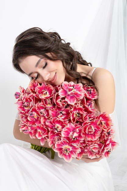 Sexy vrouw met bloemen roze tulpen in handen op een lichte achtergrond