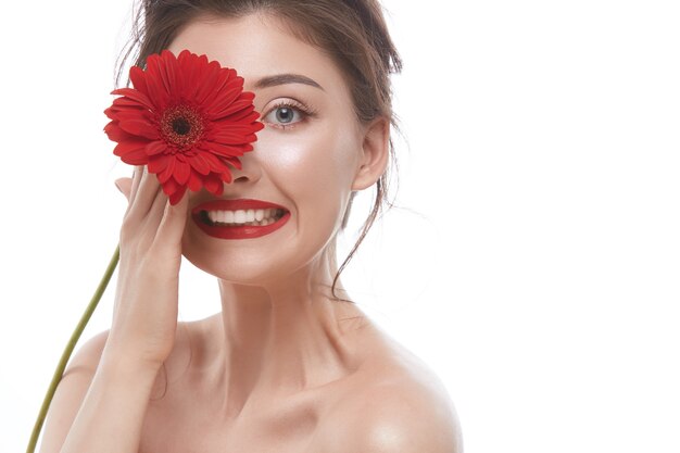 Sexy vrouw smilng naar de camera en één oog sluiten met rode bloem geïsoleerd op rood