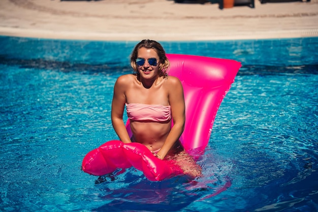 Sexy vrouwelijk model in zonnebril rusten en zonnebaden op een matras in het zwembad Vrouw in een roze bikinizwempak drijvend op een opblaasbare roze matras spf en zonnebrandcrème