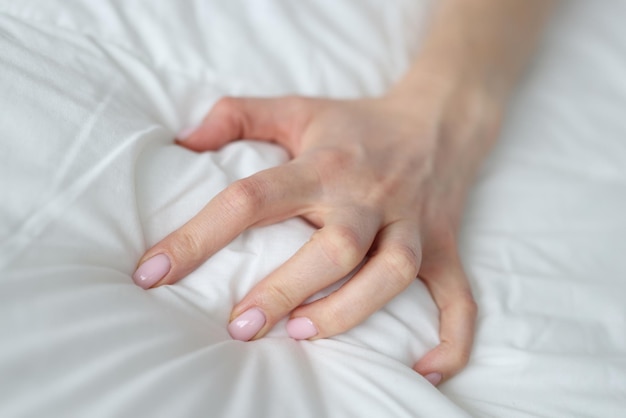 Sexy vrouwelijke hand trekken en knijpen witte lakens in bed