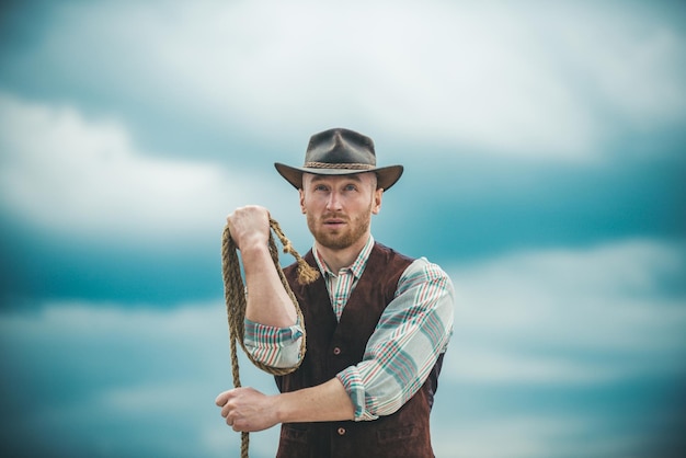 Sexy western man with cowboy hat Cowboy with lasso rope on sky background