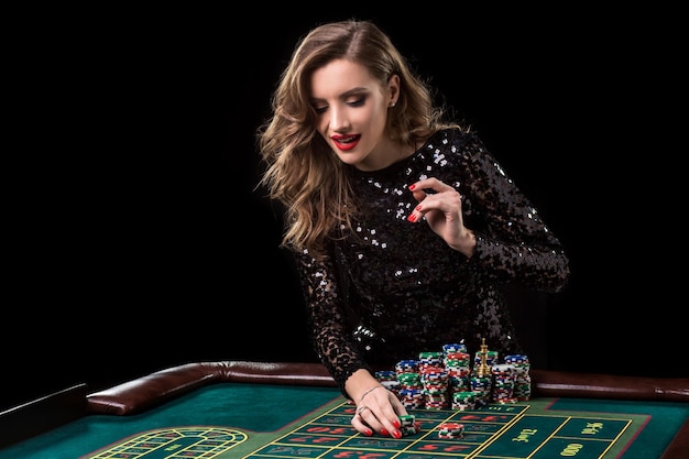 Donna sexy in un vestito nero che gioca nel casinò. la donna punta pile di fiches giocando alla roulette al club del casinò. gioco d'azzardo. roulette.