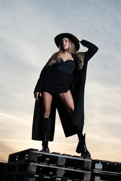 검은 패션 코트 모자와 검은 신발 부츠에 섹시 한 여자 패션 드레스 야외에서 아름 다운 젊은 여자 섹시 하 고 관능적인 여성 모델