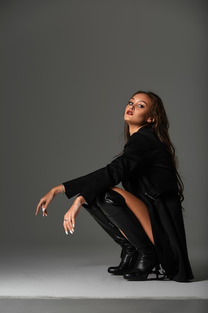 Sexy woman in black swimsuit and black high boots Fashion young woman with long legs posing at studio