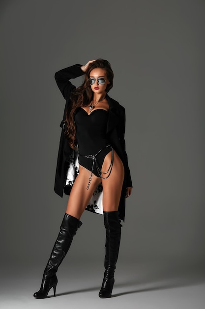 Sexy woman in black swimsuit and black high boots Fashion young woman with long legs posing at studio