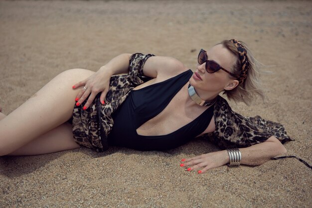 Sexy woman in a black swimsuit and sunglasses is lie on the beach in summer