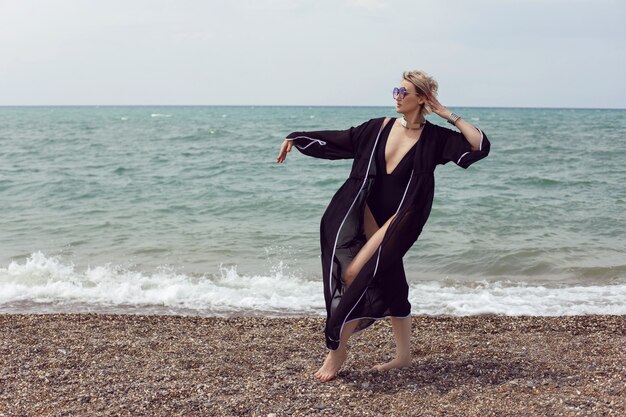 Sexy woman in a black swimsuit and sunglasses is stand on the beach in summer