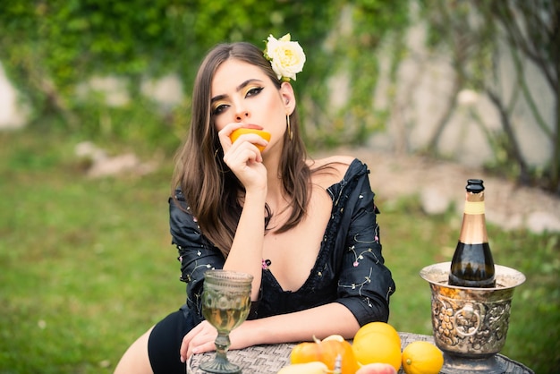 Sexy woman eating orange outdoor young pretty girl on summer picnic on a grass in the park with wine