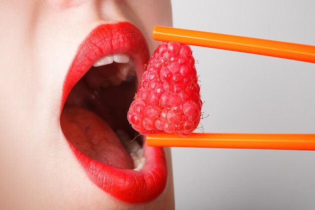 The sexy woman eats  a raspberry by chopsticks and holds it near lips