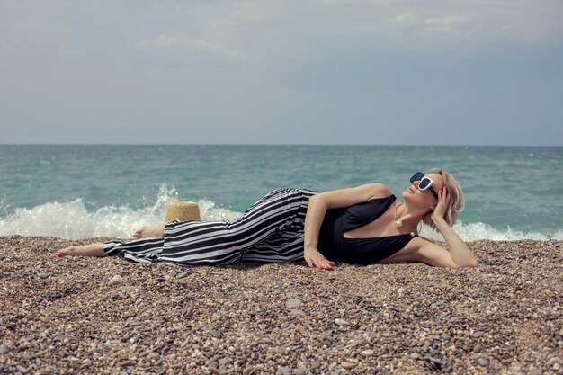 Фото Сексуальная женщина в черном купальнике, полосатых штанах и солнцезащитных очках лежит на пляже