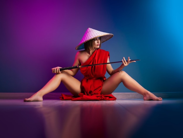 写真 赤いマントとアジアの帽子をかぶったセクシーな女性の手に刀を持ったネオンカラーの侍のイメージ