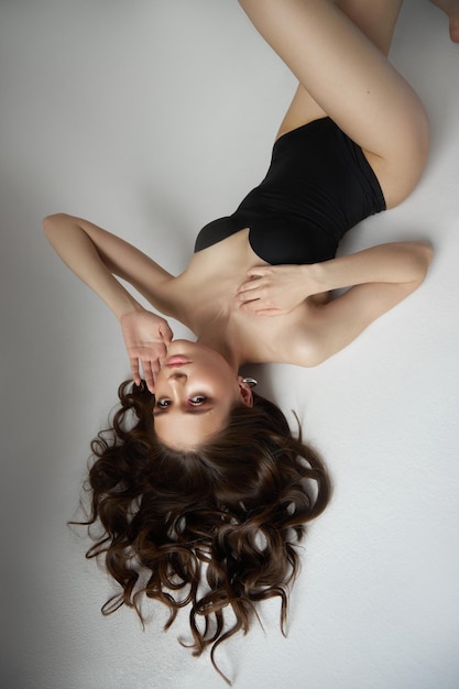 Sexy woman lying on the floor in a black bodysuit studio portrait Perfect body the figure of a young woman