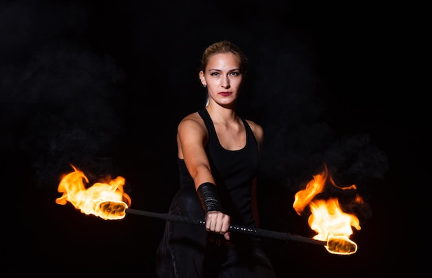 Sexy woman performer twirl burning baton during fire performance in dark night outdoors partying