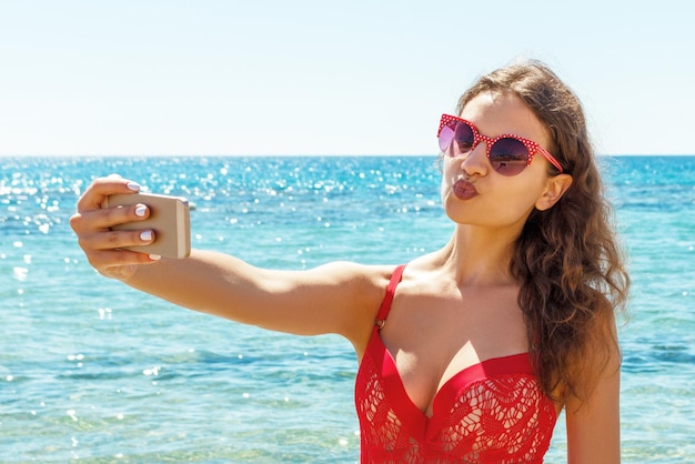 Sexy woman in red swimwear is taking selfie at the sea background Beach concept