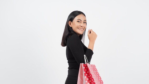 セクシーな女性の買い物。白で隔離赤い買い物袋を保持している黒を身に着けている美しい少女