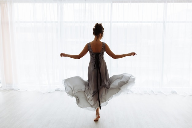 Sexy woman in transparent dress against window, back view, room in white tones on background