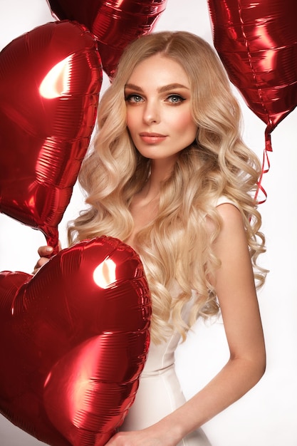 Photo sexy woman in white dress and balloons with hearts posing in the studio on valentine's day