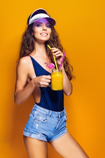 Sexy Woman in white swimsuit and blue jeans shorts, trendy visor holding beverage