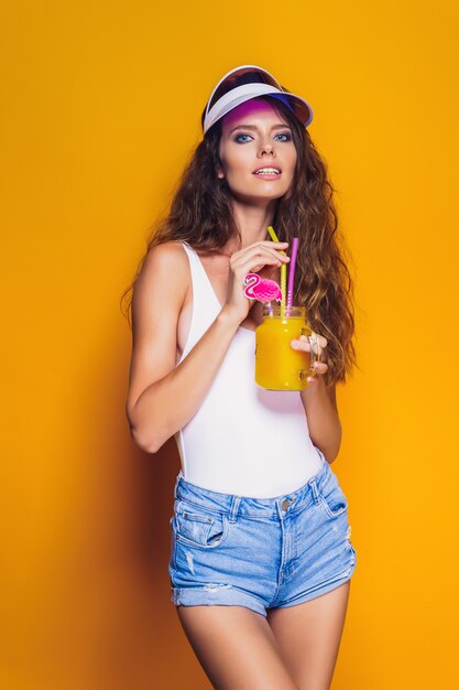 Sexy Woman in white swimsuit and blue jeans shorts, trendy visor holding beverage