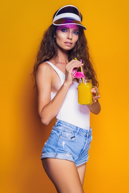 Sexy Woman in white swimsuit and blue jeans shorts, trendy visor holding beverage