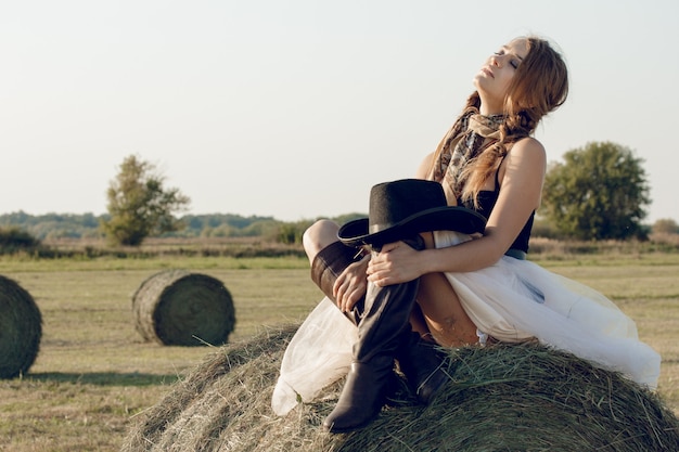 Sexy woman with cowboy hat and dress at haystack resting after work