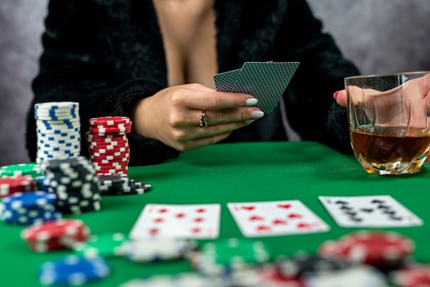 Sexy woman with poker cards and chips in hands playing poker at the table