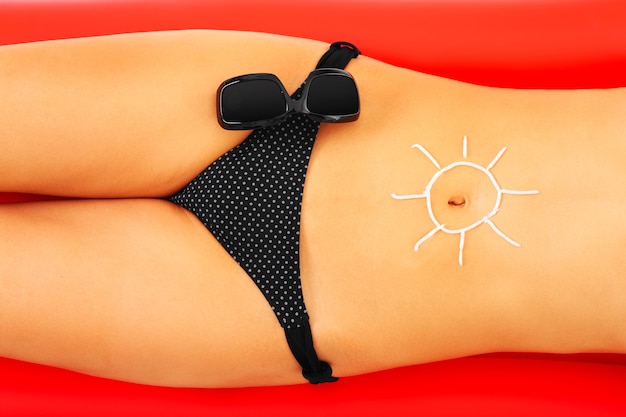 Photo a sexy woman with a sun symbol on belly made of sunscreen on a red mattress