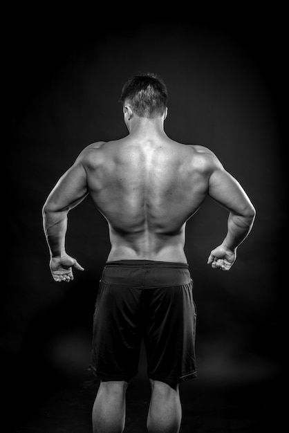 Sexy young athlete posing on a black space in the Studio. Fitness, bodybuilding, black and white.