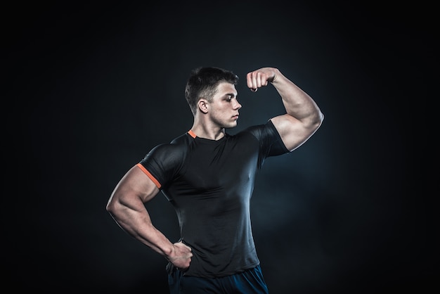 Sexy young athlete posing on a black wall . Fitness, bodybuilding