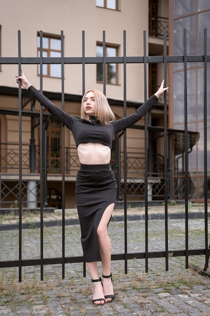 Sexy young blonde woman in black crop top on metal fence background Sexy young woman in the city