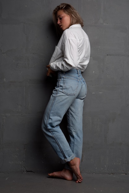 Sexy young blonde woman in an unbuttoned shirt and jeans on a dark background