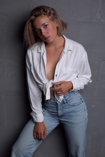 Sexy young blonde woman in an unbuttoned shirt and jeans on a dark background