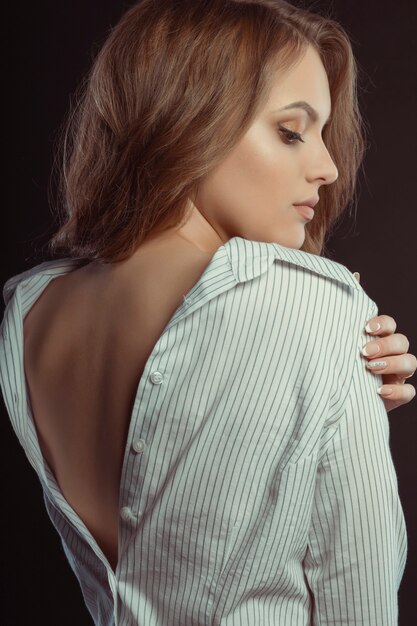 Sexy young brunette woman posing in white men's shirt at studio