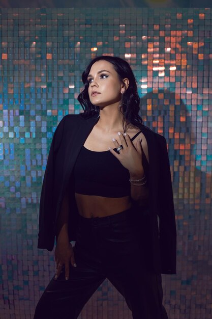 Sexy young energetic woman in black suit in the studio against a background of shiny squares