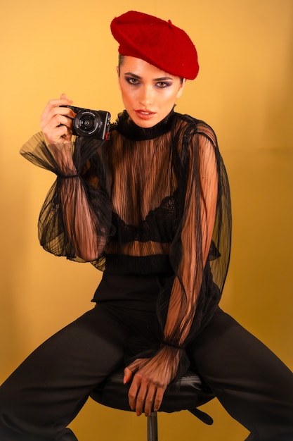 A sexy young female in a red beret hat and a black transparent shirt holding the camera