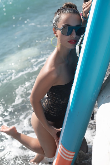 세련된 선글라스를 끼고 바다 옆에 있는 수프 보드에 수영복을 입은 섹시한 어린 소녀