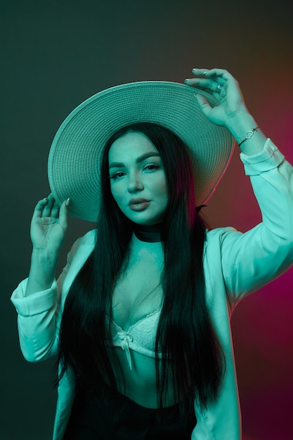 Sexy young woman on a colorful wall. Brunette model girl in  sexy clothes and hat in neon light.