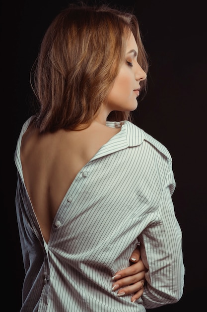 Sexy young woman posing in men's shirt with naked back