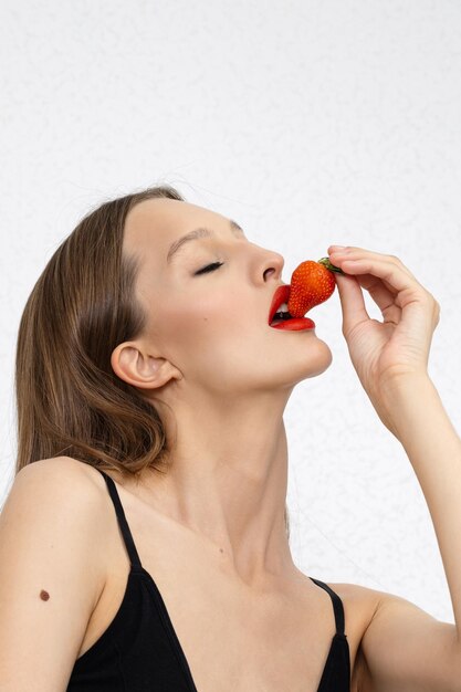 Foto giovane donna sexy con la fragola sul primo piano bianco del fondo