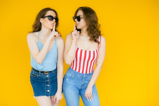Sexy zorgeloze vrouwen poseren in de buurt van gele muur in zonnebril Positieve modellen gaan