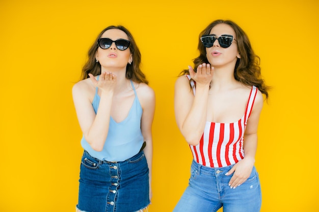 Sexy zorgeloze vrouwen poseren in de buurt van gele muur in zonnebril Positieve modellen gaan