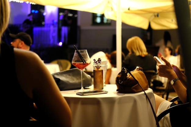 Sfeer van een avondcafé er staat een cocktail op tafel het meisje zit met haar rug naar de camera en luistert naar muziek horizontale foto