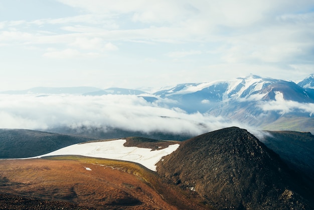 Sfeervol alpine landschap met gigantische lage wolk boven rotsachtige berg met gletsjer. Grote dikke wolk boven hoogland vallei. Prachtig landschap op grote hoogte. Vliegen over bergen boven wolken.