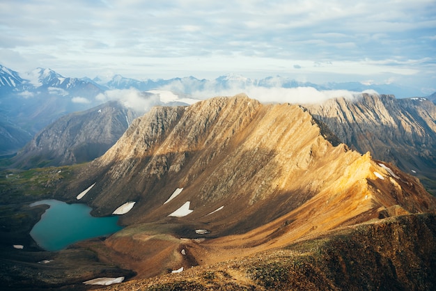 Sfeervol alpine landschap tot lage wolken op grote gouden puntige rockies in zonlicht. Reuzenbergen met gletsjer, gouden rots met puntige piek en bergmeer in hooglandvallei. Prachtig landschap.