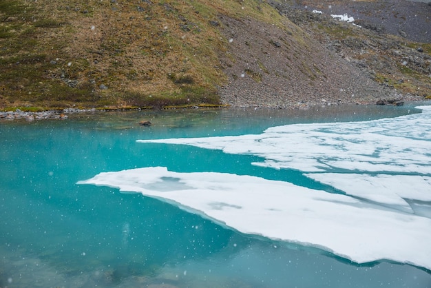 Sfeervol berglandschap met bevroren bergmeer tijdens sneeuwval Helder ijs drijft op wateroppervlak van meer Geweldig berglandschap met ijskoud bergmeer Sneeuwvlokken op waterachtergrond