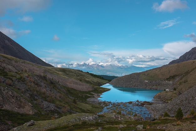 Sfeervol landschap met azuurblauw bergmeer tegen hoge sneeuwwitte bergketen in zonlicht in lage wolken Dramatisch avondzicht op alpenmeer en grote zonovergoten sneeuwbergen in lage wolken