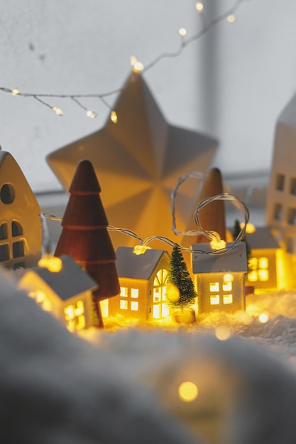 Sfeervol miniatuur winterdorp Stijlvolle keramische huisjes en houten kerstbomen op sneeuwdeken met gloeiende lichten in de moderne kerstachtergrond Fijne feestdagen