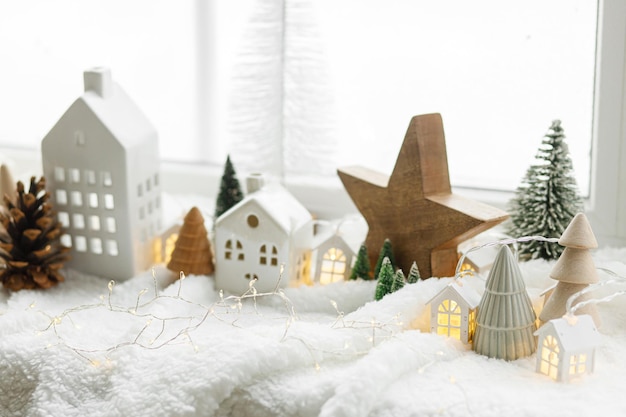 Sfeervol miniatuur winterdorp Stijlvolle schattige keramische huisjes en houten kerstbomen op zachte sneeuwdeken met gloeiende lichten Kerst moderne witte achtergrond Fijne feestdagen